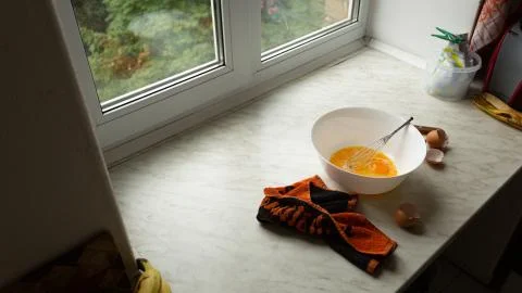 Bowl of raw eggs on the kitchen table by the window, top view Photos