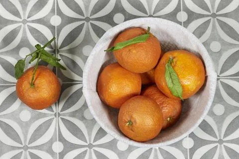Bowl of ripe mandarin sits on a patterned tile surface with a few extra oranges  Stock Photos