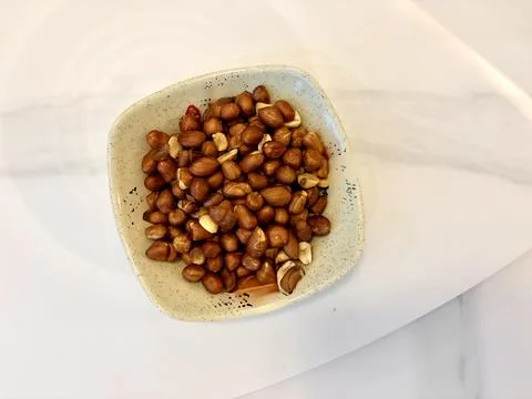 A bowl of roasted hazelnuts on a white surface. Fotos de archivo