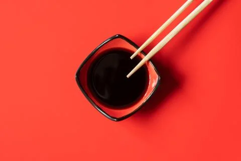 Bowl of soy sauce and wooden chopsticks on red background.  Stock Photos