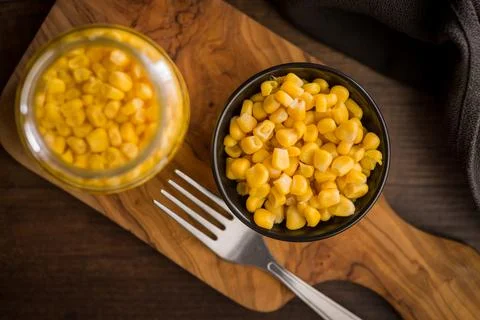 Bowl Of Sweet Corn Kernels With Fork On Wooden Cutting Board Next To Jar. Stock Photos