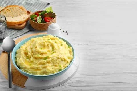Bowl of tasty mashed potatoes with greens served on white wooden table. Space Stock Photos