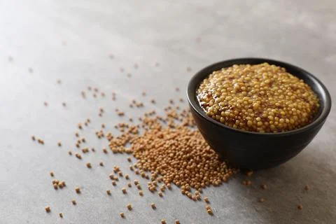 Bowl of whole grain mustard and seeds on grey table Stock Photos