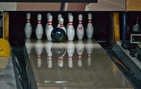 Bowling ball hitting and knocking down white pins in the alley. Stock Photos