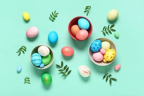 Bowls with painted Easter eggs and leaves on turquoise background Stock Photos