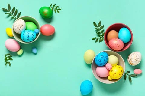 Bowls with painted Easter eggs and leaves on turquoise background Stock Photos