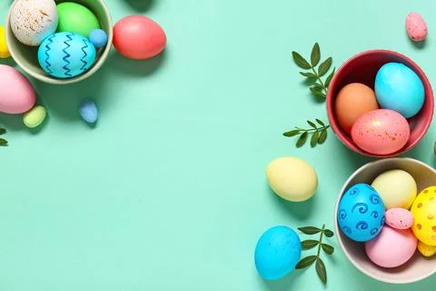 Bowls with painted Easter eggs and leaves on turquoise background Stock Photos