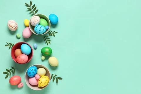 Bowls with painted Easter eggs and leaves on turquoise background Stock Photos