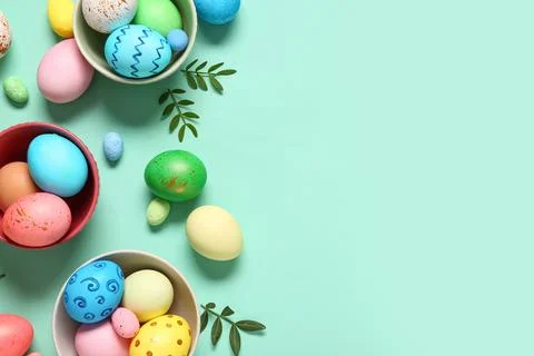 Bowls with painted Easter eggs and leaves on turquoise background Stock Photos
