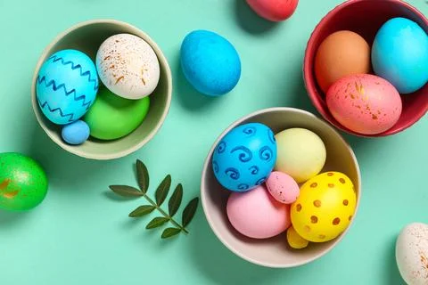 Bowls with painted Easter eggs and leaves on turquoise background Stock Photos