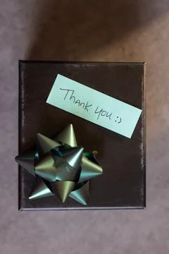 A box with a bow on top and a note that says "Thank you" written on it Stock Photos