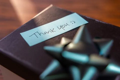A box with a bow on top and a note that says "Thank you" written on it Stock Photos