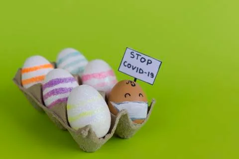 Box with decoratively painted shiny easter eggs and one egg wearing medical m Stock Photos