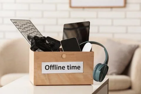 Box with different devices and text OFFLINE TIME on table at home, closeup. D Stock Photos