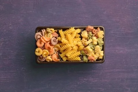 A box with different types of raw pasta lies on a wooden table Stock Photos