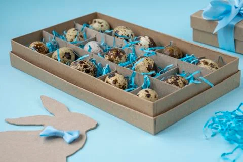 Box with Easter eggs, an Easter Bunny and a gift on a blue background. Creati Stock Photos