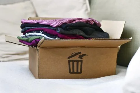 Box with folded clothes marked with trash bin icon as concept for textile waste Stock Photos