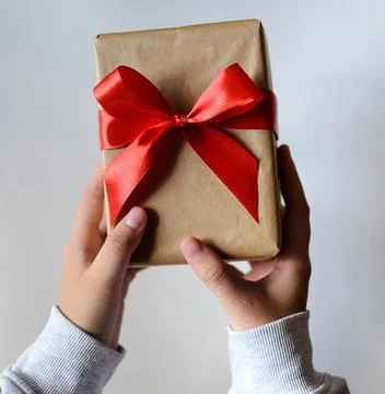 A box, a gift with a red bow in hands. Stock Photos