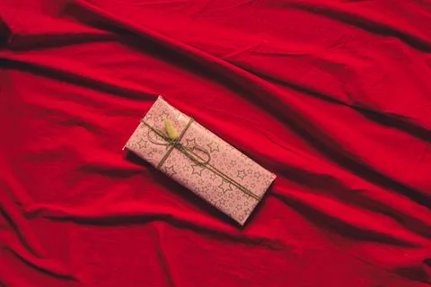 Box with a gift on a red tablecloth on the table at home, a gift for a birthd Stock Photos