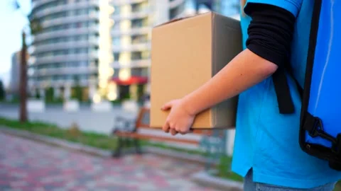 A box in the hands of a deliveryman against the backdrop of an unrecognizable Stock Footage 235796533