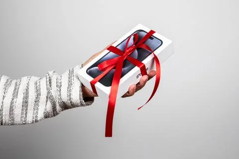 Box of the Iphone 15 Pro. Gift with a red ribbon in the hand on a white Stock Photos