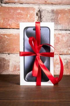 Box of the Iphone 15 Pro on a red brick background. Gift with a red ribbon Stock Photos