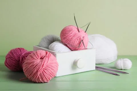 Box with knitting yarn and needles on wooden table against green wall Stock Photos
