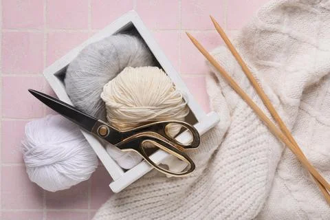 Box with knitting yarn, scissors, needles and sweater on pink tile background Stock Photos