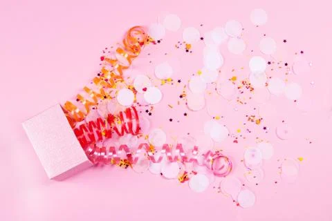 Box on pink background with multicolored serpantine and confetti. Stock Photos