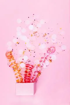 Box on pink background with multicolored serpantine and confetti. Stock Photos