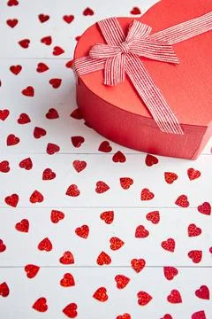 Boxed gift placed on heart shaped red sequins on white wooden table Valent... 스톡 사진