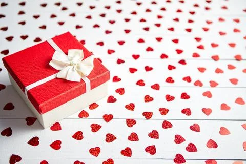 Boxed gift placed on heart shaped red sequins on white wooden table Valent... 스톡 사진