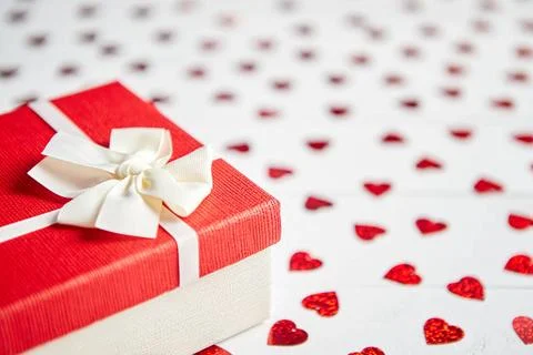 Boxed gift placed on heart shaped red sequins on white wooden table Valent... 스톡 사진