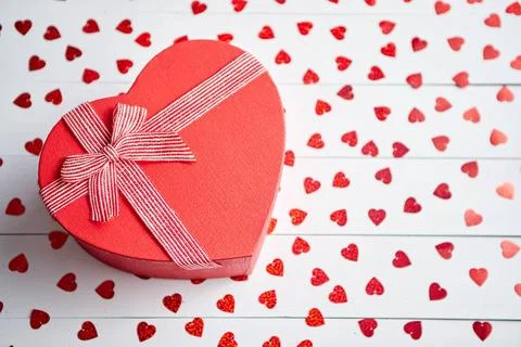 Boxed gift placed on heart shaped red sequins on white wooden table Valent... 스톡 사진