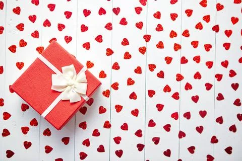 Boxed gift placed on heart shaped red sequins on white wooden table Valent... 스톡 사진