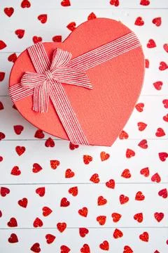 Boxed gift placed on heart shaped red sequins on white wooden table Valent... 스톡 사진