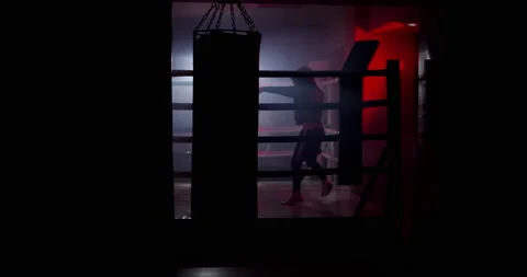 A boxer boxing with a shadow draws quick punches in a semi-dark ring with a back Stock Footage 157898504