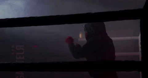 A boxer boxing with a shadow draws quick punches in a semi-dark ring with a back Stock Footage 157898662
