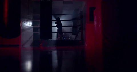 A boxer boxing with a shadow draws quick punches in a semi-dark ring with a back Stock Footage 157898902
