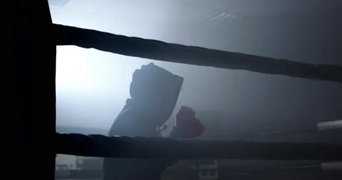 A boxer boxing with a shadow draws quick punches in a semi-dark ring with a back Stock Footage 157899022