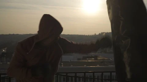 Boxer with fighting gloves stands in guard punches bag in sunset, close up, city Stock Footage 98499367