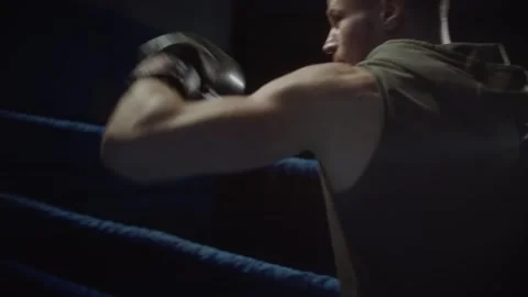 Boxer man hits boxing gloves punching bag in dark gym. Close up fighter workout Stock Footage 315564009