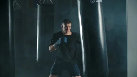 Boxer practicing punch with bag in smoky gym Stock Footage 309962283