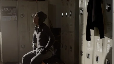 Boxer sitting on bench focused in musty locker room with hoodie on 스톡 동영상 104545947