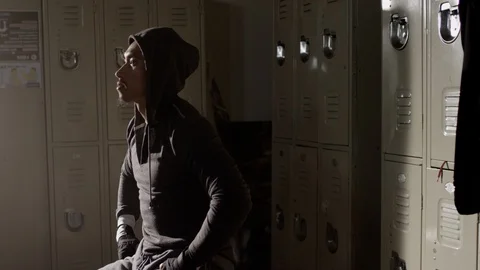 Boxer sitting on bench focused in musty locker room with hoodie on 스톡 동영상 104546194
