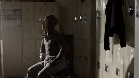 Boxer sitting on bench focused in musty locker room with hoodie on 스톡 동영상 104548532