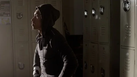 Boxer sitting on bench looking up in musty locker room with hoodie on Vídeos de archivo 104542895