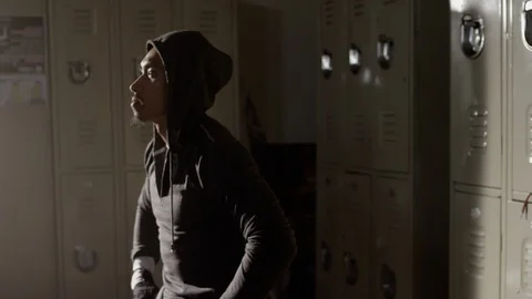Boxer sitting on bench looking up in musty locker room with hoodie on Stock Footage 104544335