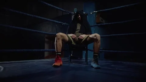 Boxer sitting on chair in ring after intense training, covering head with towel Stock Footage 315563943