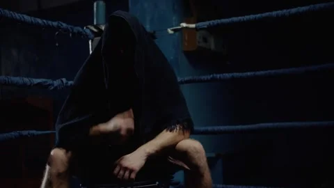 Boxer sitting on chair in ring after intense training, covering head with towel Stock Footage 315563968